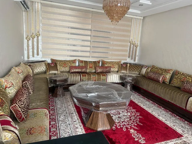 صالون مغربي بيج على شكل U بوسائد عنابية وزربية حمراء